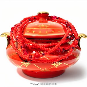 May include: A bright red ceramic lidded bowl with gold-colored handles and gold star-like patterns, topped with a coiled necklace of red beads and dark red faceted crystals. The text "www.ritualscent.com" is printed at the bottom of the image.