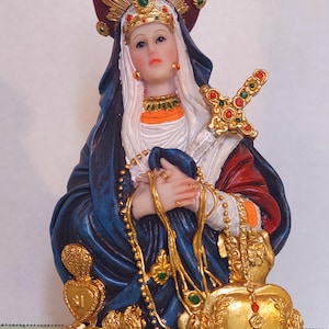 May include: A religious figurine of a woman in a blue robe, holding a sword and rosary. The statue has a gold crown and accents, with a red base and a halo. The figure has a serene expression.