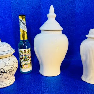 Puede incluir: Un tarro de cerámica blanca con tapa estampada, una botella de colonia Florida Water con etiqueta dorada, un tarro de jengibre de cerámica blanca alto con tapa puntiaguda y un tarro de jengibre de cerámica blanca con textura acanalada.