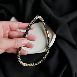 Op de afbeelding: Een zwarte en gouden kralenketting met een magneetsluiting.