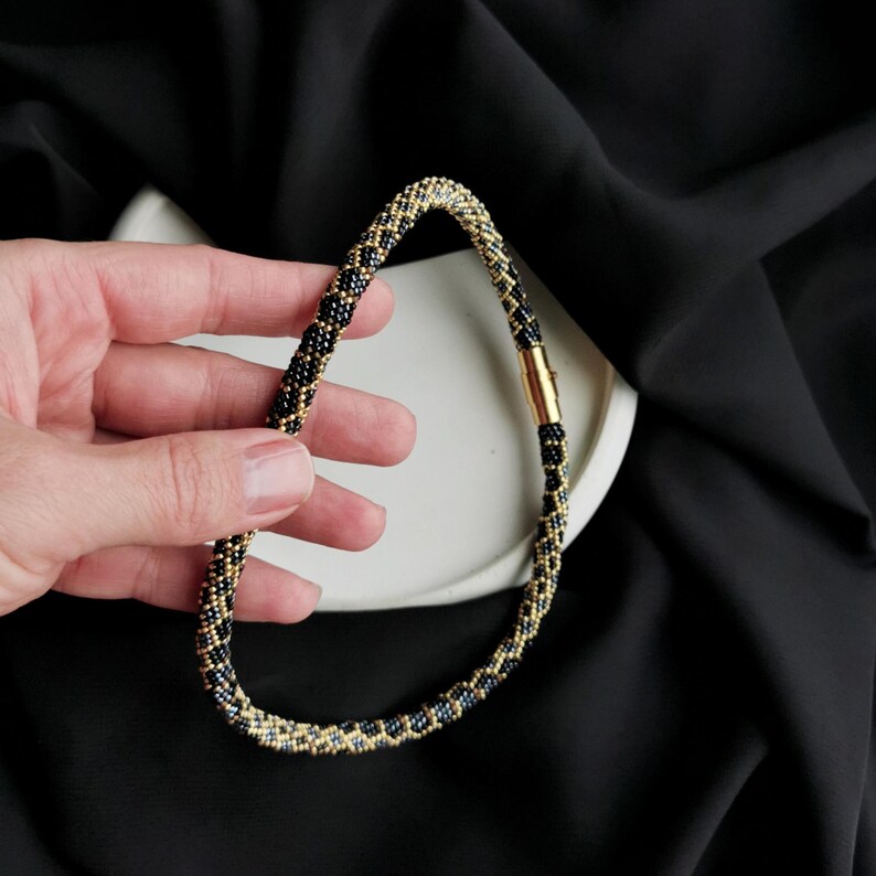 Op de afbeelding: Een zwarte en gouden kralenketting met een magneetsluiting.