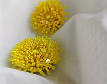 May include: Two yellow beaded flower-shaped earrings. The earrings are made of small, round beads that are clustered together to form a flower shape.