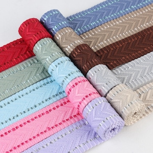 May include: Assortment of woven ribbon trim with a chevron pattern and silver accents. The ribbon trim comes in a variety of colors including light blue, pink, lavender, brown, beige, and gray.