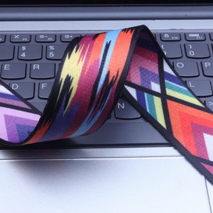 May include: A colorful woven strap with a geometric pattern in shades of red, orange, yellow, blue, green, purple, and black. The strap is lying on a laptop keyboard.