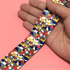 May include: A colorful patterned ribbon with geometric shapes in shades of red, blue, yellow, white, and brown.