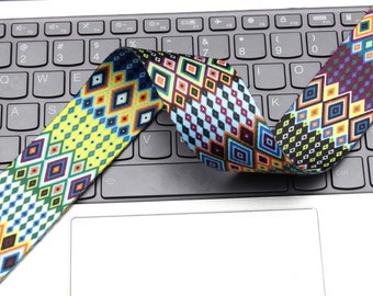 Op de afbeelding: Een kleurrijk geweven band met een geometrisch ontwerp in tinten blauw, geel, rood, groen en zwart. Het band is gevouwen en geplaatst op een laptoptoetsenbord.