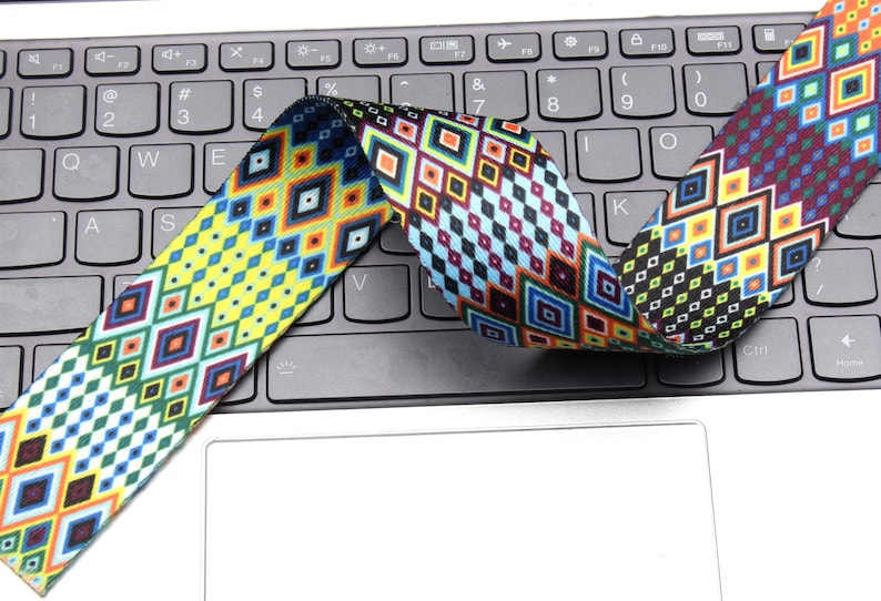 May include: A colorful patterned woven strap with a geometric design in shades of blue, yellow, red, green, and black. The strap is folded and placed on a laptop keyboard.