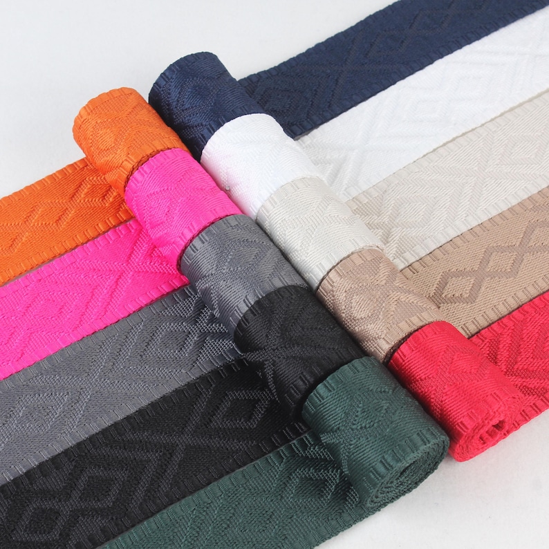 May include: Assortment of woven webbing in various colors, including orange, pink, gray, black, green, and red. The webbing has a diamond pattern and is rolled up.