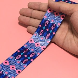 Può includere: Nastro elastico blu con un motivo geometrico rosa, blu e bianco.
