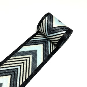 May include: Black and white chevron patterned ribbon with blue and cream accents. The ribbon is rolled up and the pattern is visible.
