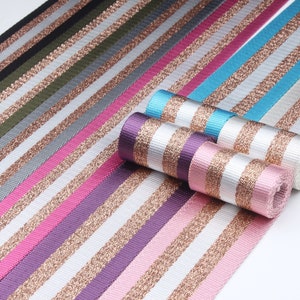 May include: A variety of striped ribbon with gold glitter accents. The ribbon is in various colors, including black, green, gray, pink, purple, and blue.
