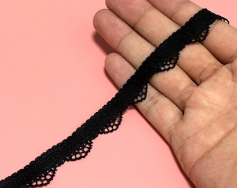 May include: Black lace trim with a scalloped edge. The trim is delicate and has a fine, intricate pattern.