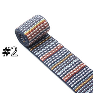 May include: A close-up of a blue, white, red, and yellow striped woven ribbon. The ribbon is rolled up and the label #2 is visible.