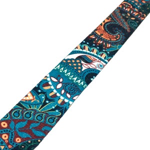 May include: A teal, orange, and brown paisley patterned ribbon. The ribbon has a white background and is made of a soft, woven fabric.