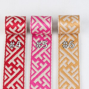 Puede incluir: Tres rollos de cinta tejida con patrones geom&eacute;tricos. La cinta es blanca con acentos rojos, rosados y dorados. Los rollos est&aacute;n etiquetados con #4, #5 y #6.