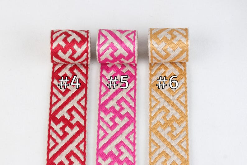 Puede incluir: Tres rollos de cinta tejida con patrones geom&eacute;tricos. La cinta es blanca con acentos rojos, rosados y dorados. Los rollos est&aacute;n etiquetados con #4, #5 y #6.