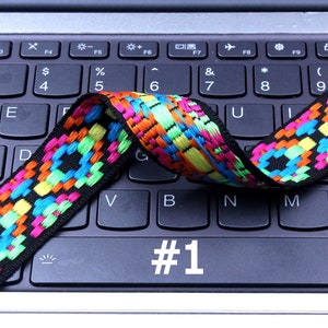 Op de afbeelding: Een kleurrijk geweven band met zwarte, blauwe, groene, gele en oranje accenten ligt over een zwart laptoptoetsenbord. De toets #1 is gemarkeerd.