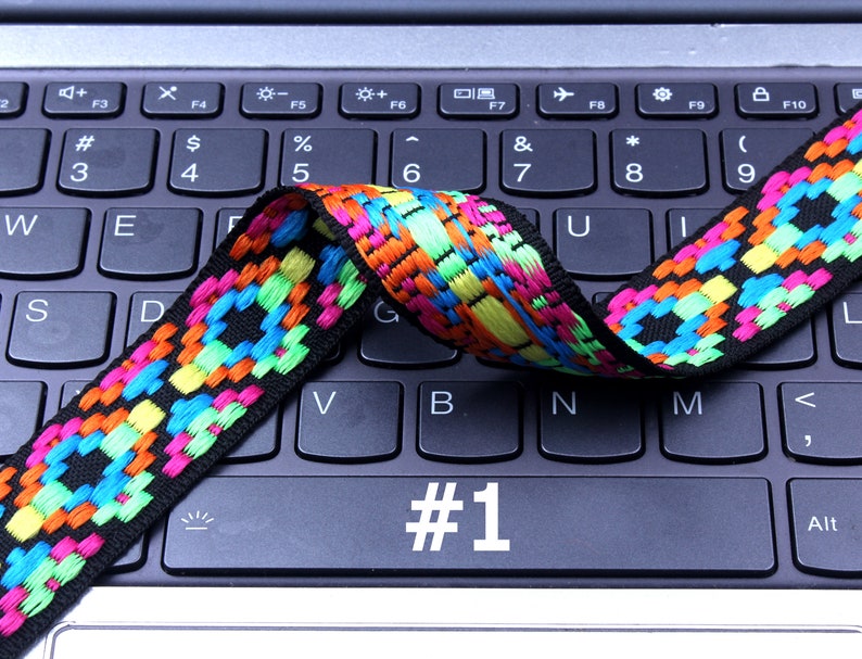 Op de afbeelding: Een kleurrijk geweven band met zwarte, blauwe, groene, gele en oranje accenten ligt over een zwart laptoptoetsenbord. De toets #1 is gemarkeerd.