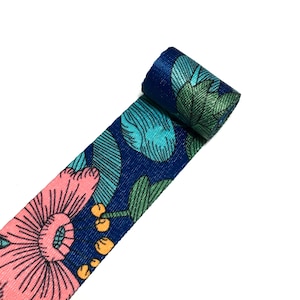 Puede incluir: Una cinta azul y verde con estampado floral y flores rosas. La cinta está enrollada y lista para ser utilizada para manualidades o decoración.