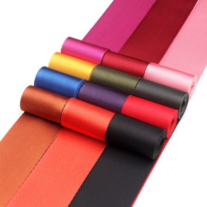 May include: Assortment of colorful nylon webbing straps in various colors, including red, orange, brown, black, purple, green, yellow, blue, pink, and burgundy. The straps are rolled up and arranged in a fan shape.