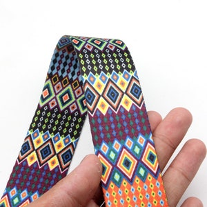 May include: A colorful patterned fabric ribbon with a geometric design featuring squares and diamonds in shades of red, blue, yellow, green, and black.