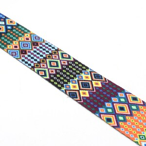 May include: A colorful patterned ribbon with a geometric design featuring squares and diamonds in shades of blue, green, yellow, orange, red, and black.