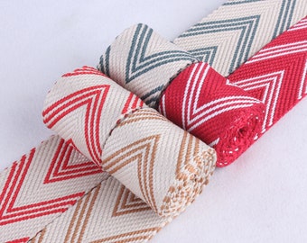 Könnte beinhalten: Drei Rollen gewebtes Stoffband mit Chevron-Muster. Das Band ist in Rot, Beige und Blau erhältlich.