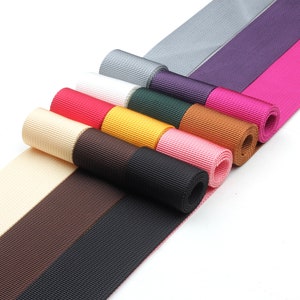 May include: A collection of ten rolls of colorful webbing in various colors, including black, brown, beige, yellow, green, pink, red, purple, gray, and pink. The webbing is arranged in a fan shape, with the ends of the rolls overlapping.