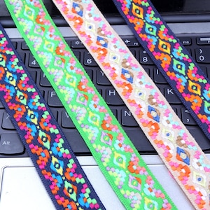 Może przedstawiać: Zbliżenie na cztery kolorowe wstążki z geometrycznymi wzorami. Wstążki mają wzory w kształcie rombów w kolorze pomarańczowym, różowym i niebieskim na granatowym, zielonym i beżowym tle. Nadaje się do rękodzieła lub dekoracji.