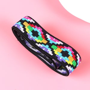 May include: A black elastic band featuring a repeating geometric pattern in vibrant colors including neon pink, bright yellow, turquoise, and purple. The woven fabric has a textured surface and is coiled into a loop, displaying a consistent design.