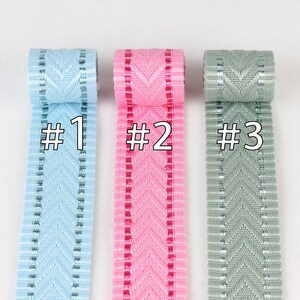 May include: Three rolls of ribbon with a chevron pattern. The ribbon is light blue, pink, and gray. The ribbon is labeled #1, #2, and #3.