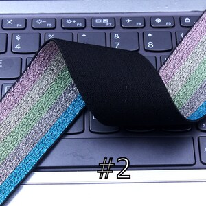 Pu&ograve; includere: Primo piano di un elastico nero con una striscia iridescente multicolore. L'elastico &egrave; piegato a met&agrave; e posizionato su una tastiera di un laptop. Il numero "#2" &egrave; scritto sulla tastiera.