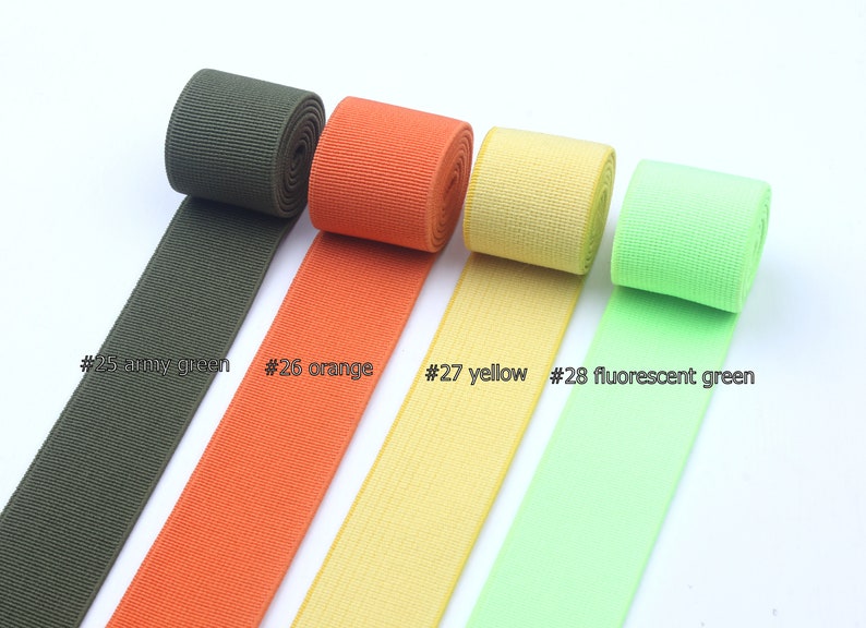 May include: Four rolls of elastic ribbon in different colors: army green, orange, yellow, and fluorescent green. The ribbon is labeled with numbers 25, 26, 27, and 28.