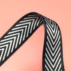 K&ouml;nnte beinhalten: Schwarz-wei&szlig;es Chevron-Musterband. Das Band ist in der Mitte gefaltet und bildet ein V.