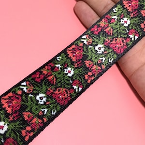 Op de afbeelding: Zwart geweven lint met een bloemenpatroon in tinten rood, groen en wit.