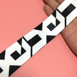 May include: White elastic webbing with a black geometric pattern. The pattern is a repeating design of interlocking shapes.