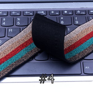 Pu&ograve; includere: Primo piano di un elastico nero con strisce dorate, rosse e turchesi. L'elastico &egrave; piegato a met&agrave; e posizionato su una tastiera di un laptop. Il numero "#4" &egrave; scritto sulla tastiera.