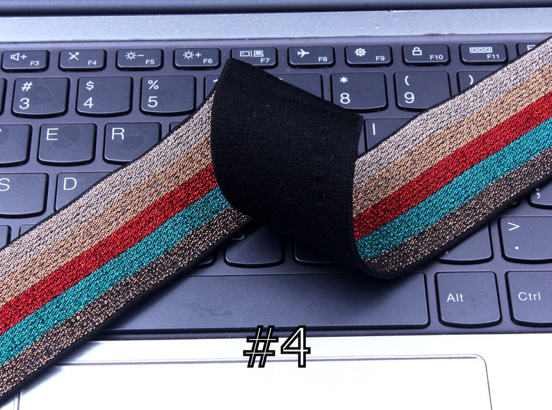Pu&ograve; includere: Primo piano di un elastico nero con strisce dorate, rosse e turchesi. L'elastico &egrave; piegato a met&agrave; e posizionato su una tastiera di un laptop. Il numero "#4" &egrave; scritto sulla tastiera.