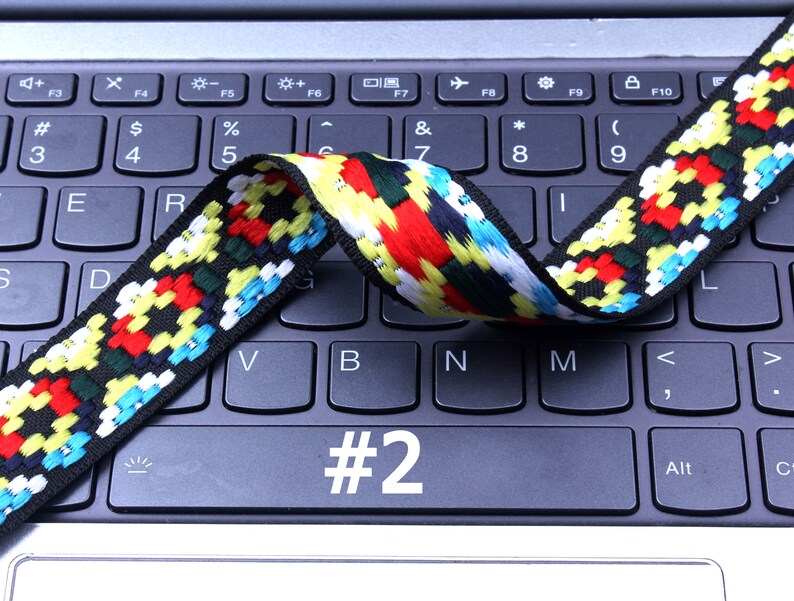 Op de afbeelding: Een kleurrijk geweven lint met zwarte, rode, gele, witte en blauwe strepen ligt over een laptoptoetsenbord. Het nummer "#2" is zichtbaar op het toetsenbord.