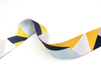 May include: A yellow, blue, and white geometric patterned ribbon. The ribbon is woven and has a subtle texture.