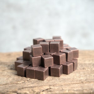 May include: A pile of small, copper-coloured cubes on a wooden surface. The cubes are arranged in a random pattern, creating a textured and geometric look.