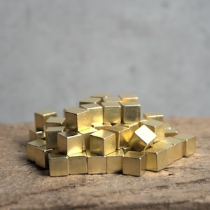 Könnte beinhalten: Ein Haufen kleiner, goldfarbener Metallwürfel auf einer Holzoberfläche.