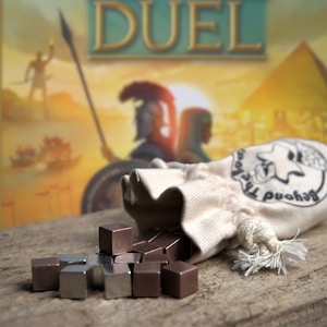 Può includere: Una borsa bianca con coulisse con il testo "Beyond The Hood" e un design a stella. La borsa sta riversando piccoli cubi di metallo, alcuni argentati e altri di rame.