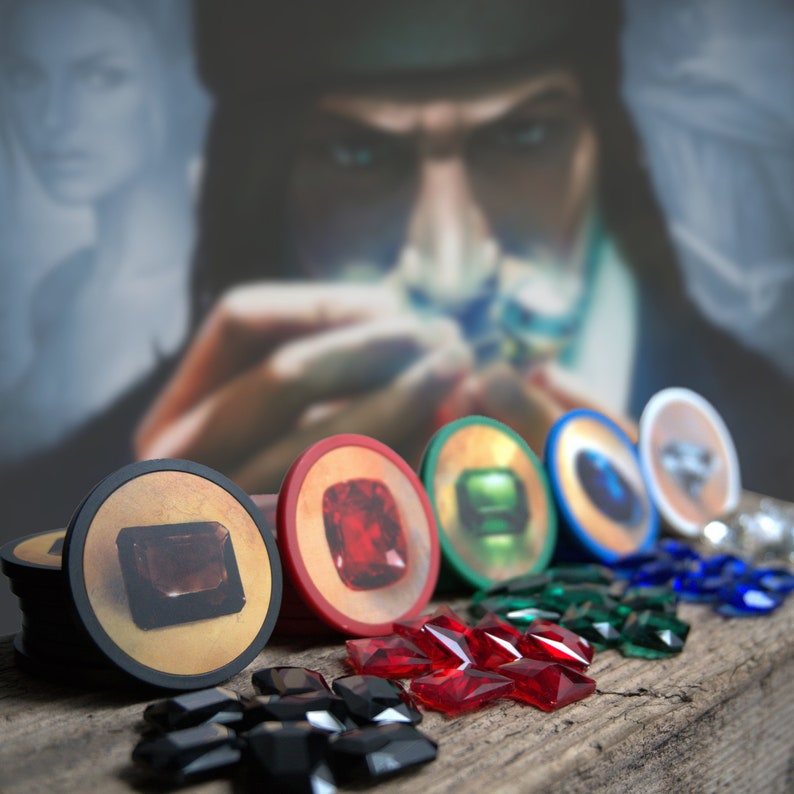 May include: A set of six colorful game pieces with different gemstone designs. The pieces are round and have a raised edge. The gemstones are red, green, blue, and brown. The pieces are arranged in a row on a wooden surface.