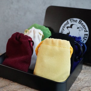 May include: A black metal box with a white logo that says "Beyond The Board EU" and contains six small velvet drawstring bags in different colors: red, white, yellow, green, black, and blue.