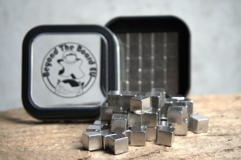 Puede incluir: Un conjunto de cubos magn&eacute;ticos plateados en un contenedor negro con el logotipo "Beyond The Board EU".