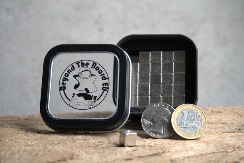 Puede incluir: Una peque&ntilde;a caja de hojalata con tapa negra y fondo de pl&aacute;stico transparente. La caja contiene un juego de peque&ntilde;os cuadrados magn&eacute;ticos plateados. La caja tiene un logotipo en la tapa que dice "Beyond The Board EU". Tambi&eacute;n hay dos monedas, una moneda de un cuarto de d&oacute;lar estadounidense y una moneda de euro, junto a la caja.