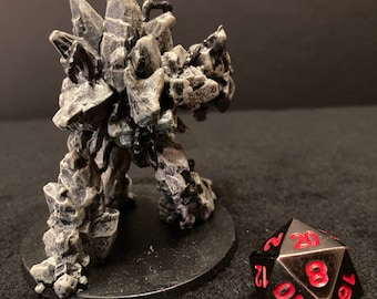 Pode incluir: Uma figura em miniatura de golem de cristal cinza e branco está em uma base preta. Um dado de metal preto de 20 lados com números vermelhos está em primeiro plano.