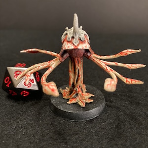 May include: A white and red painted miniature of a creature with a spiky head and multiple tentacles. The creature is standing on a black base.
