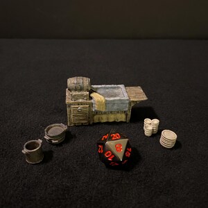 May include: A miniature wooden table with a barrel, a sink, and a wooden countertop. There are three small metal pots, a stack of white ceramic plates, and a black and silver 20-sided die with red numbers.